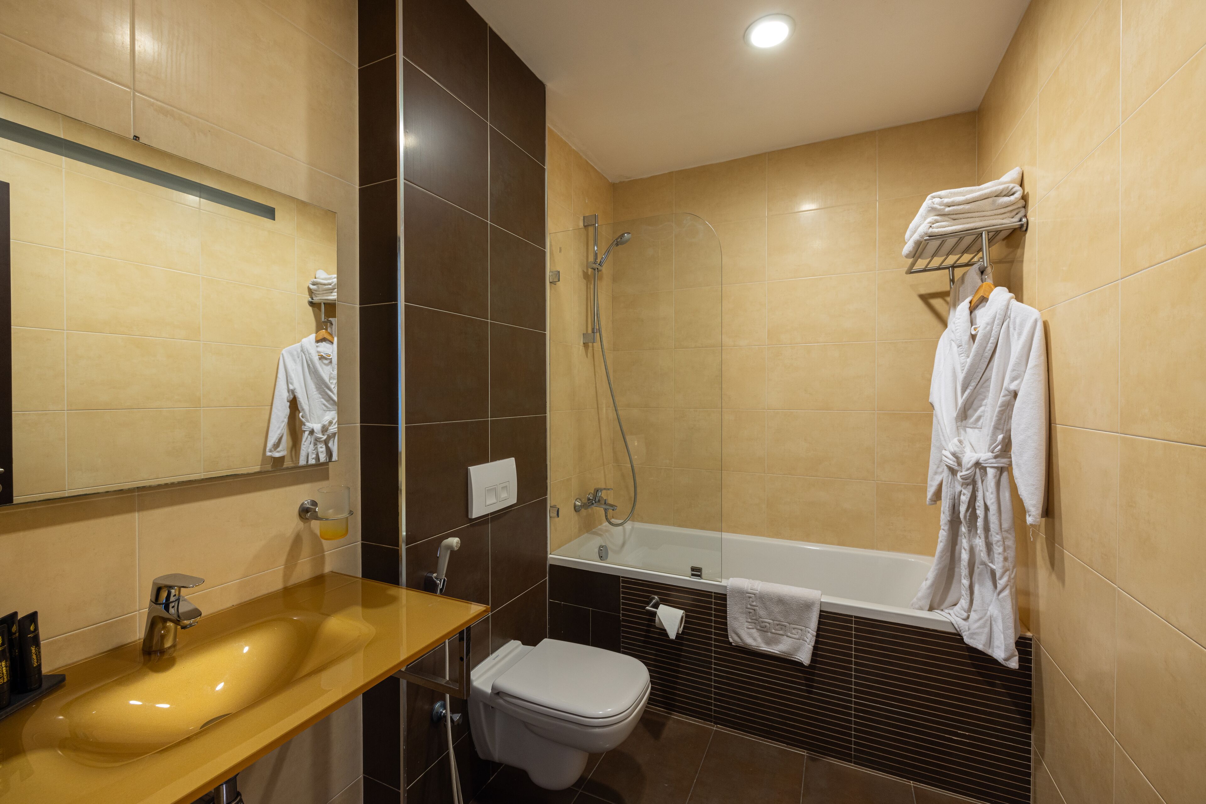 Un bany modern amb una paret revestida de rajoles beix, una banyera blanca, un lavabo amb mirall i un vàter.