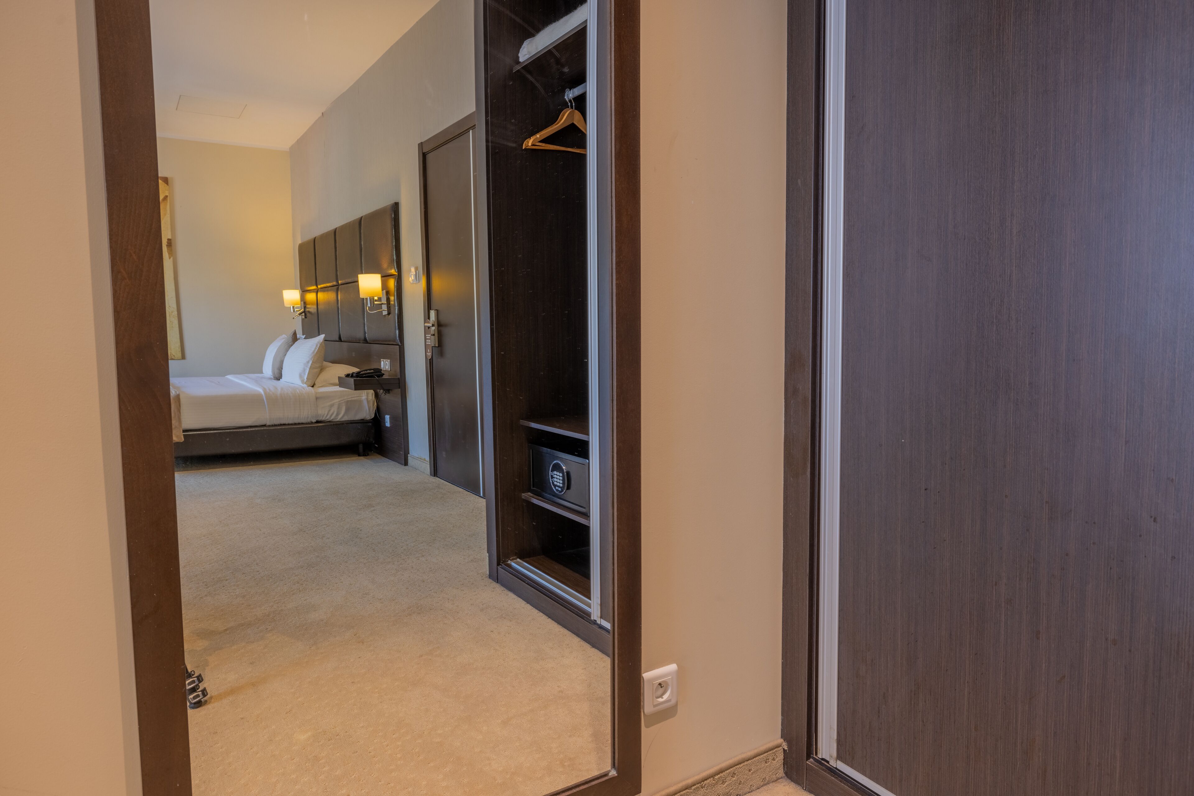A hotel room with a bed, bedside table, lamp, and a wardrobe.