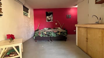 A room with a bed, a small table with a vase, a red wall, a wooden cabinet, and an air conditioning unit.