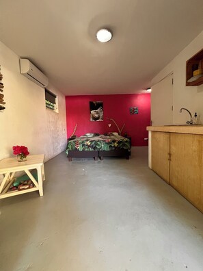 Quarto com cama, uma pequena mesa com um vaso, parede vermelha, armário de madeira e aparelho de ar condicionado.