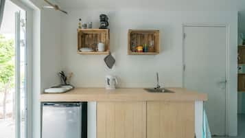 A compact kitchen with wooden cabinets, a built-in dishwasher, and two wooden shelves above the countertop.