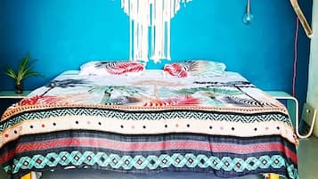 A bed with a patterned bedspread, a macrame wall hanging, and a hanging light fixture.