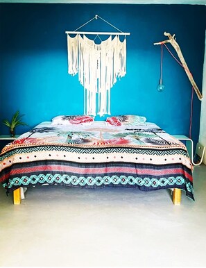 Una cama con una colcha estampada, un tapiz de macramé y una lámpara colgante.
