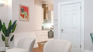 Een moderne woonkamer met twee grijze fauteuils, een grote groene plant en een kunstwerk in een lijst aan de muur.