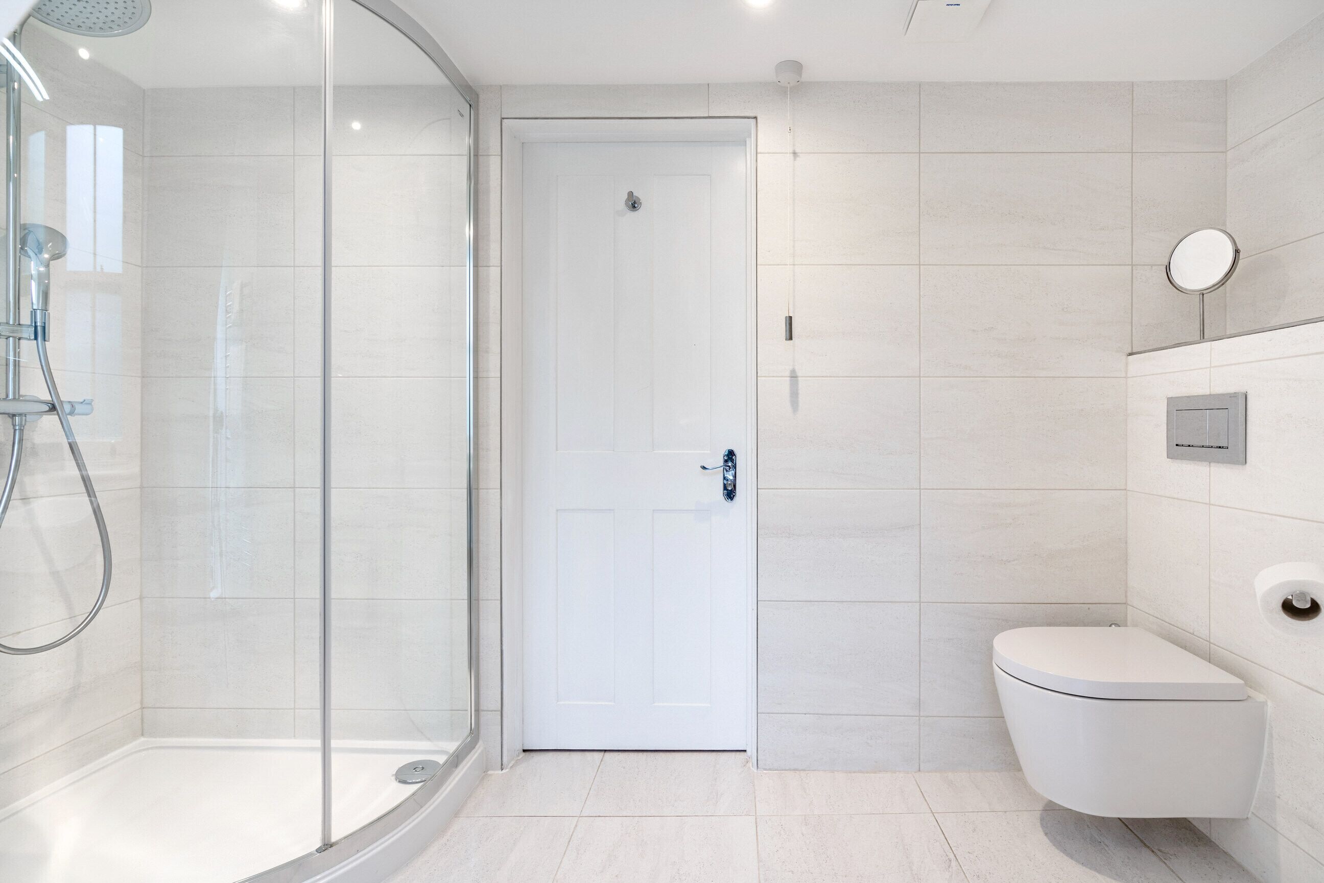 Un baño moderno con ducha de vidrio, inodoro blanco y lavamanos empotrado en la pared.