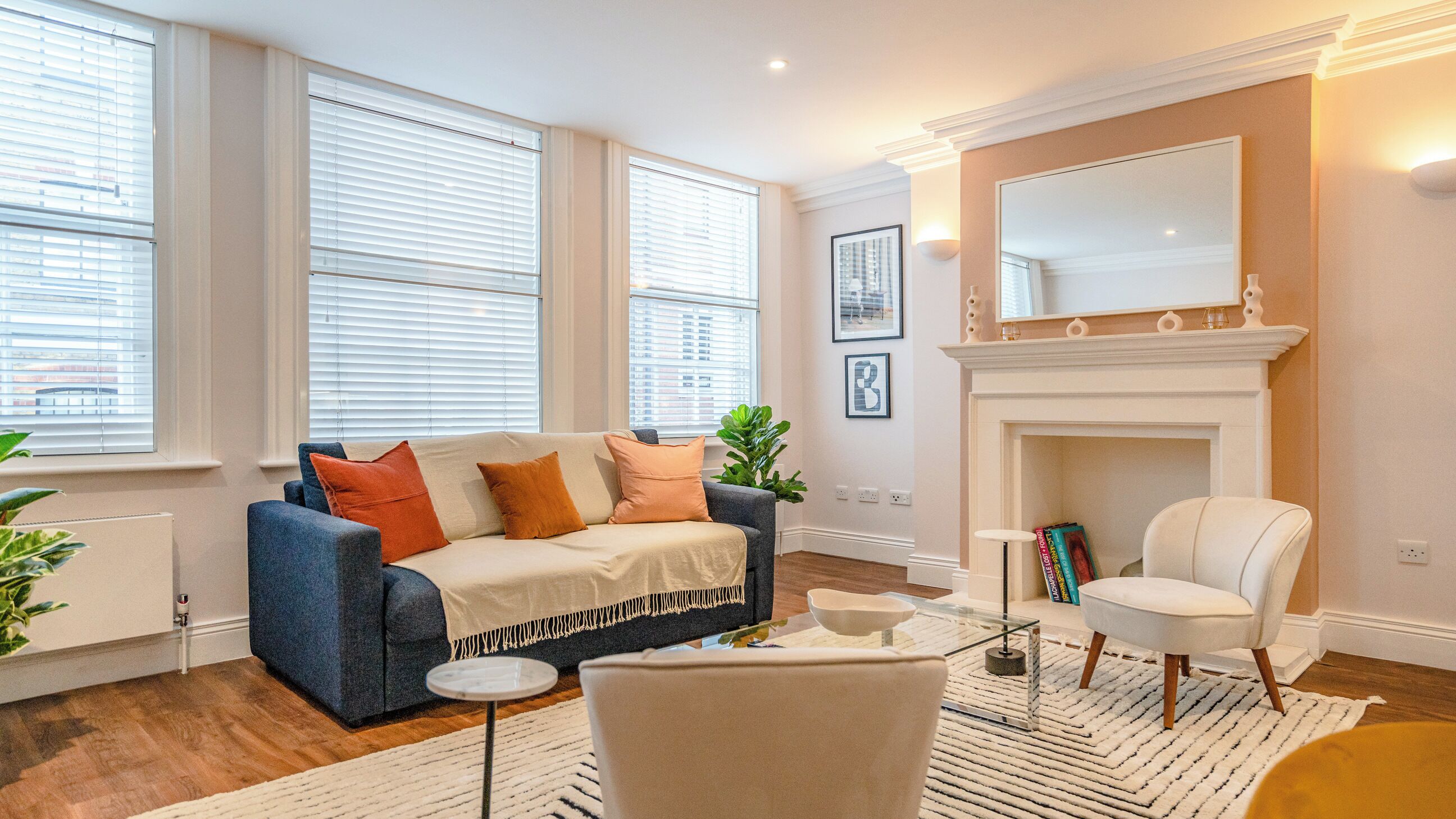 A living room with a blue sofa, a white armchair, a fireplace, and large windows.