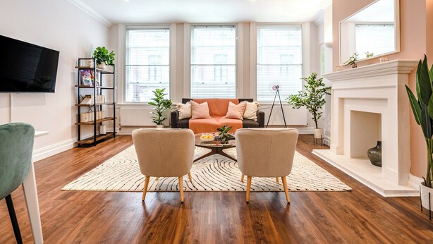 Een woonkamer met een bank, twee fauteuils, een salontafel, een boekenkast, een televisie en een open haard.