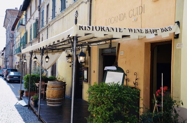 Relax in the charming outdoor seating area, sheltered by a traditional European-style awning, amidst lush greenery and rustic accents.
