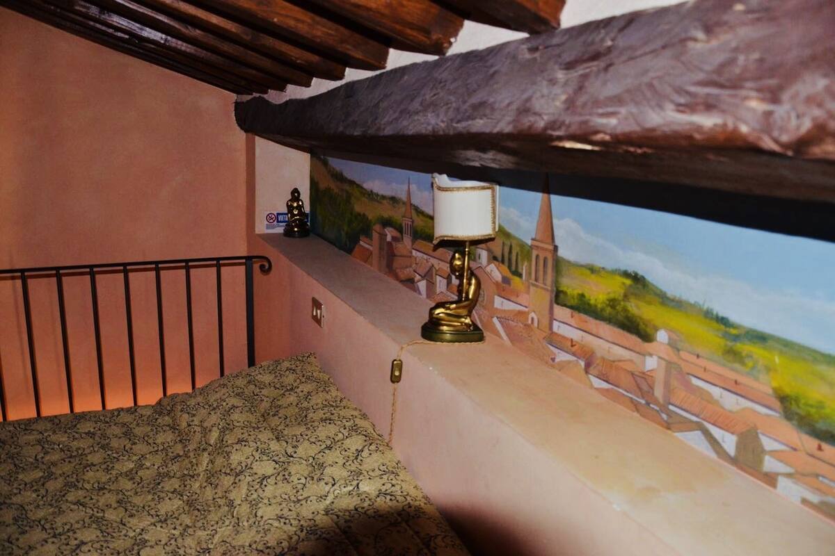 A small, cozy room with a patterned bed, a lamp, and a scenic mural on the wall.