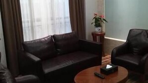 A living room with a dark brown leather sofa, a matching armchair, and a wooden coffee table with a remote control on it. - Delin Hotel (Shenzhen)