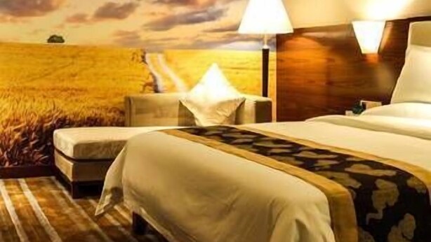 A hotel room with a large bed, a nightstand, a lamp, and a view of a field through the window. - Delin Hotel (Shenzhen)