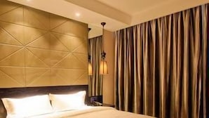 Quarto de hotel com uma cama grande, cabeceira com padrão geométrico e cortina na janela.