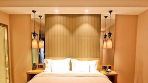Quarto de hotel com uma cama grande, duas mesinhas de cabeceira e uma luminária na parede.