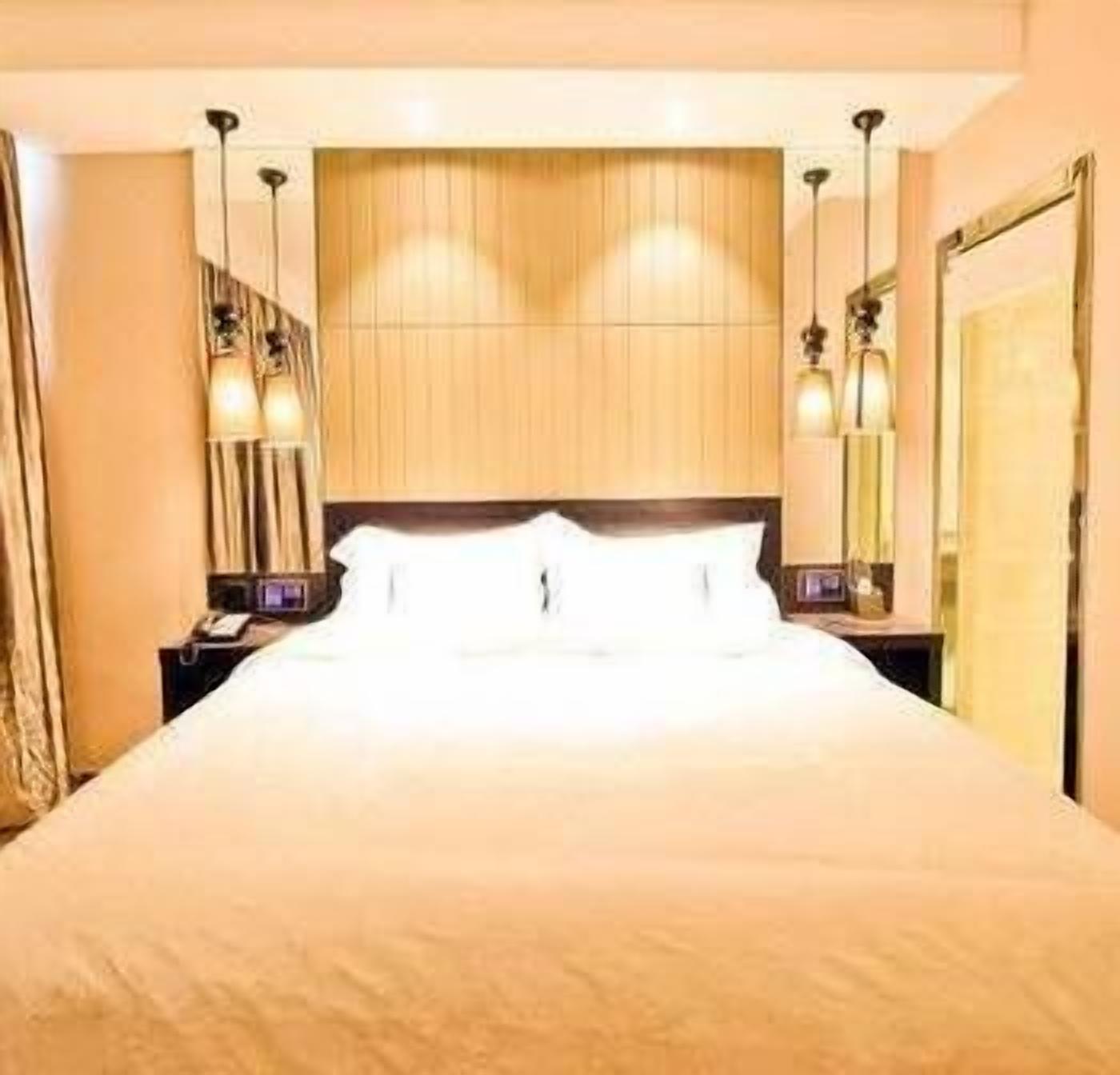 Ein Hotelzimmer mit einem großen Bett, zwei Nachttischen mit Lampen und einem Spiegel an der Wand.