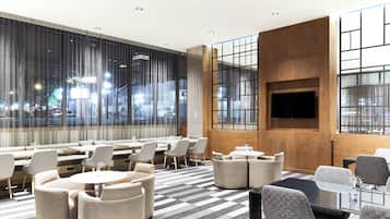 Un hall d’hôtel moderne offrant différents types de sièges, notamment des canapés, des tables rondes et des tabourets de bar. De grandes fenêtres permettent d’admirer le paysage urbain.