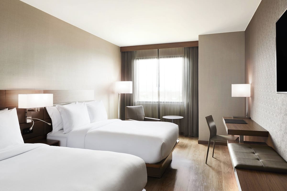 Une chambre d’hôtel avec deux lits, un bureau, une chaise et une petite table.
