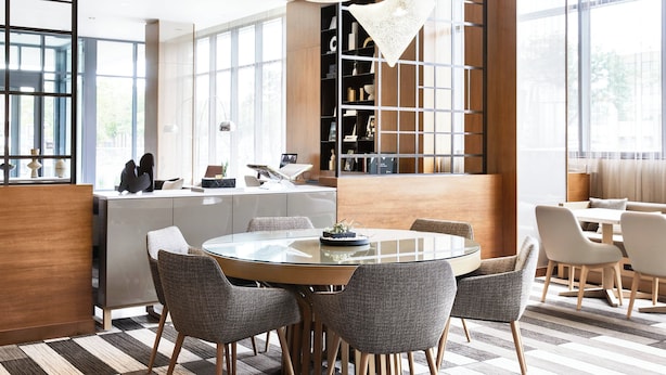 A modern dining area with a round glass table, grey upholstered chairs, and a contemporary chandelier.