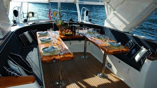 A boat's deck with a dining table set for four, surrounded by cushioned seating. - Yatch Suite Punta Ala (Castiglione della Pescaia)