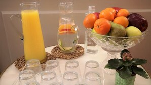 A table with a pitcher of orange juice, a glass pitcher with fruit slices, a bowl of fruit, and several shot glasses. - Casa Balmes (Barcelona)