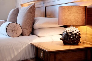 Una cama bien hecha con una mesita de noche de madera a un lado, con una lámpara y un objeto decorativo.
