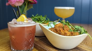 A glass of iced beverage with a lemon slice, a bowl of breaded chicken with greens, and a glass of orange juice on a wooden table.