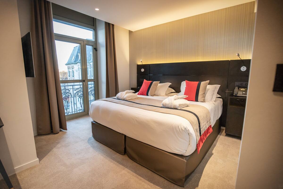 A modern hotel room with a large bed, a bedside table, a built-in TV, and a view of the outside balcony.