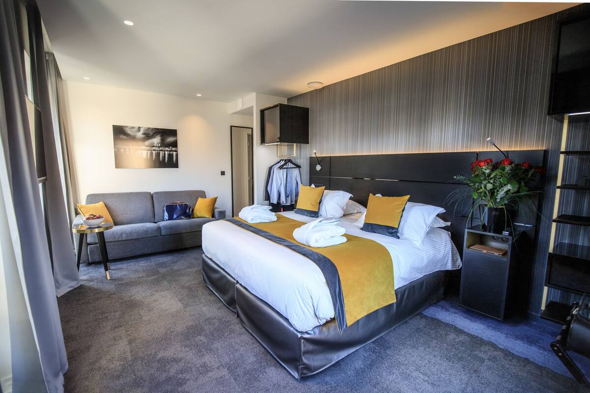 A modern hotel room with a large bed, a sofa, a small table, and a TV.
