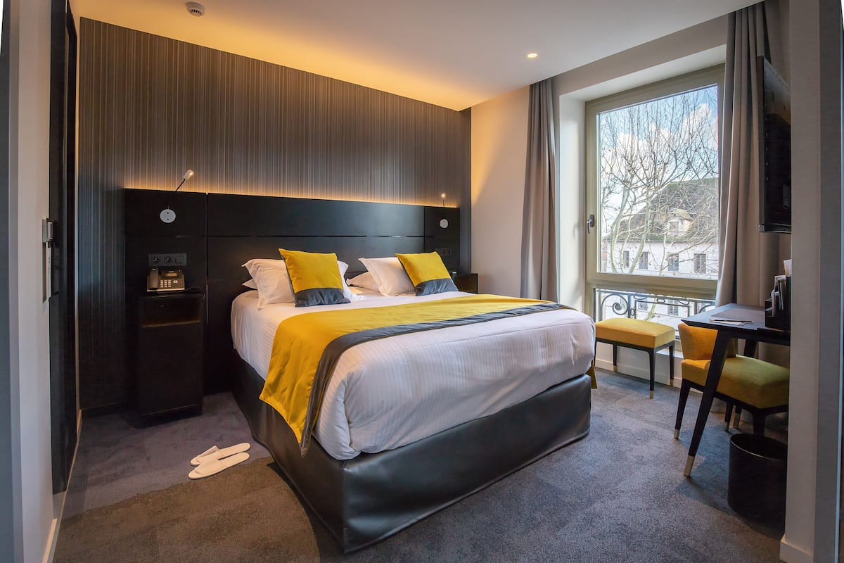 A modern hotel room with a large bed, bedside tables, a desk, and a view of the outside.
