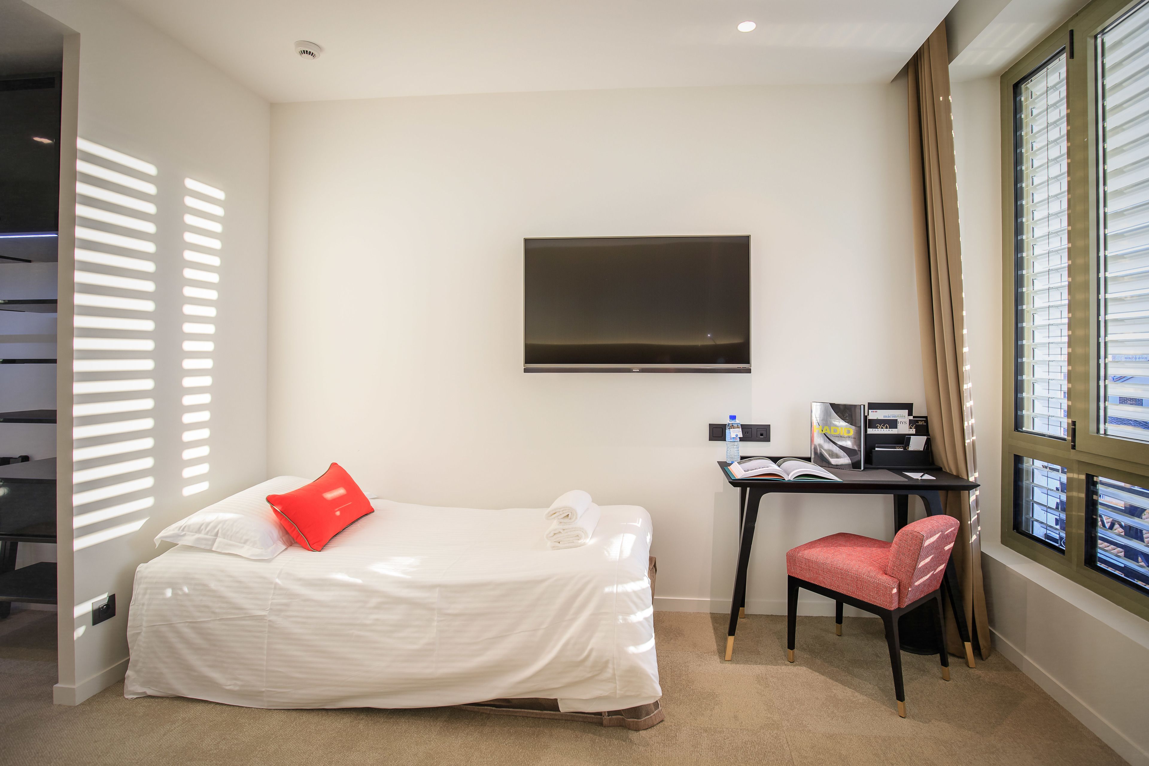 A hotel room with a bed, a desk, a chair, a TV, and a window with blinds.