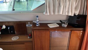 A compact kitchen area with a wooden countertop, a small refrigerator, a microwave, and a sink. There is a window above the sink with a view of boats and water. - Yacht Suite Porto Ercole (Monte Argentario)