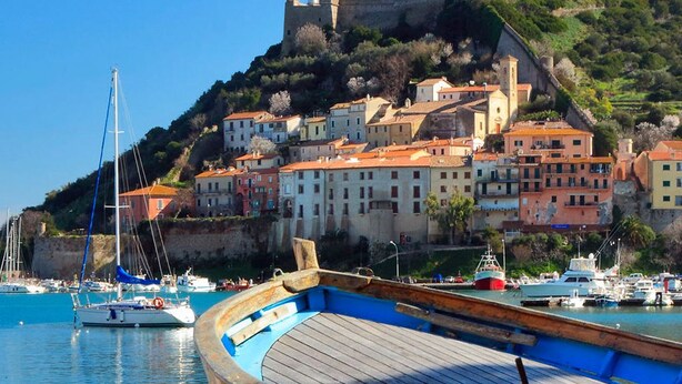 A coastal town with historic buildings, a fort on a hill, and boats in the harbor. - Yacht Suite Porto Ercole (Monte Argentario)