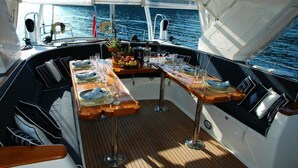 A boat's deck with a dining table set for four, surrounded by cushioned seating. - Yacht Suite Porto Ercole (Monte Argentario)