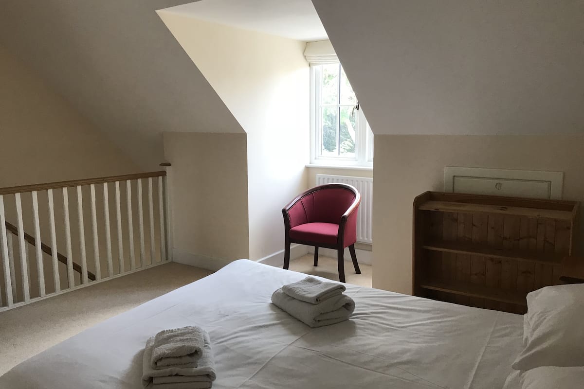 A bedroom with a sloped ceiling, a white bed with folded towels, a red chair, and a wooden cabinet.