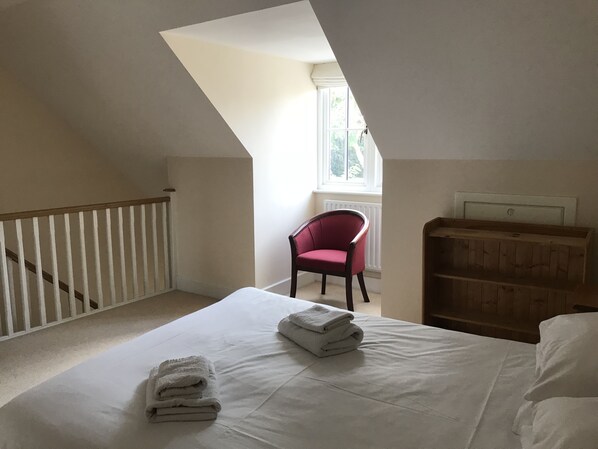 A bedroom with a sloped ceiling, a white bed with folded towels, a red chair, and a wooden cabinet. - Turi House (Canterbury)
