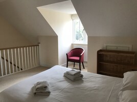 Un dormitorio con techo inclinado, una cama blanca con toallas dobladas, una silla roja y un armario de madera.