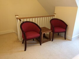 A corner room with a white radiator, two red upholstered chairs, and a small wooden table.