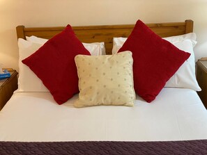 A neatly made bed with red and white pillows, a beige polka-dotted pillow, and a dark brown quilt. - Turi House (Canterbury)