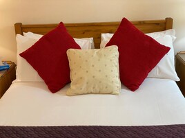 Una cama bien hecha con almohadas rojas y blancas, una almohada beige con lunares y un edredón marrón oscuro.