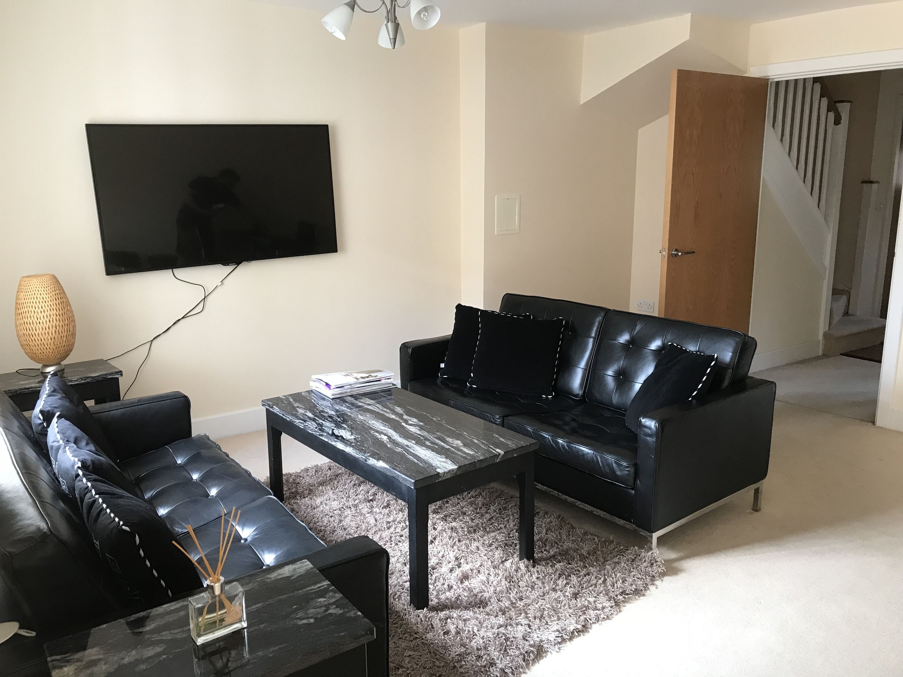 A modern living room with a black leather sofa, a coffee table, and a flat-screen TV mounted on the wall.