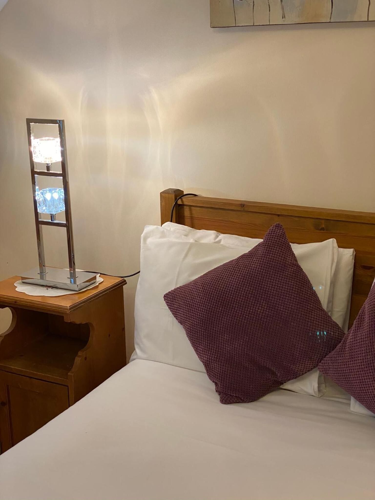 A hotel room with a wooden headboard, a bedside table with a lamp, and two pillows.