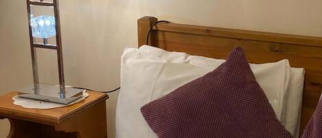 A hotel room with a wooden headboard, a bedside table with a lamp, and two pillows.