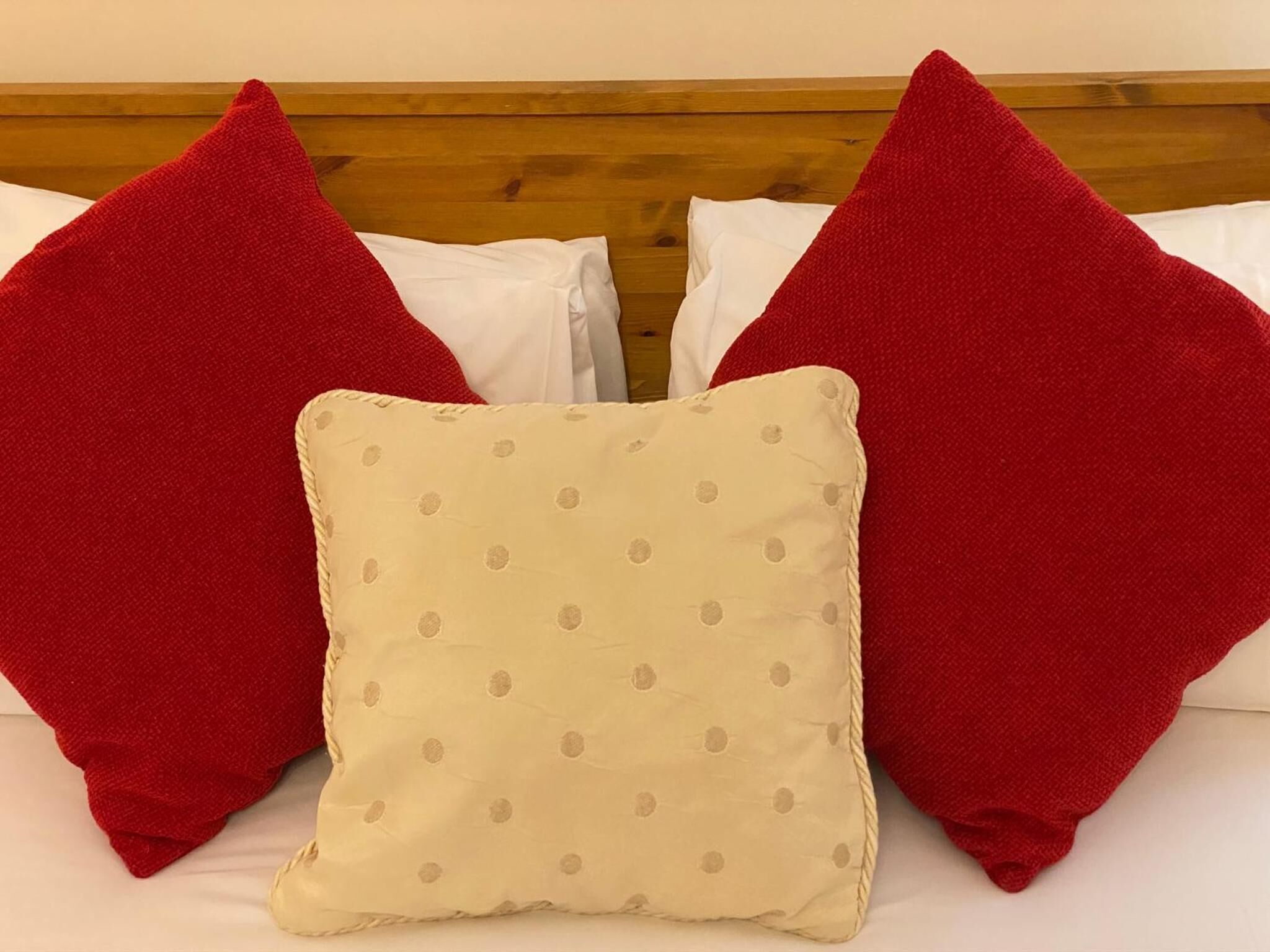 A bed with two red pillows and one beige pillow with a polka dot pattern.