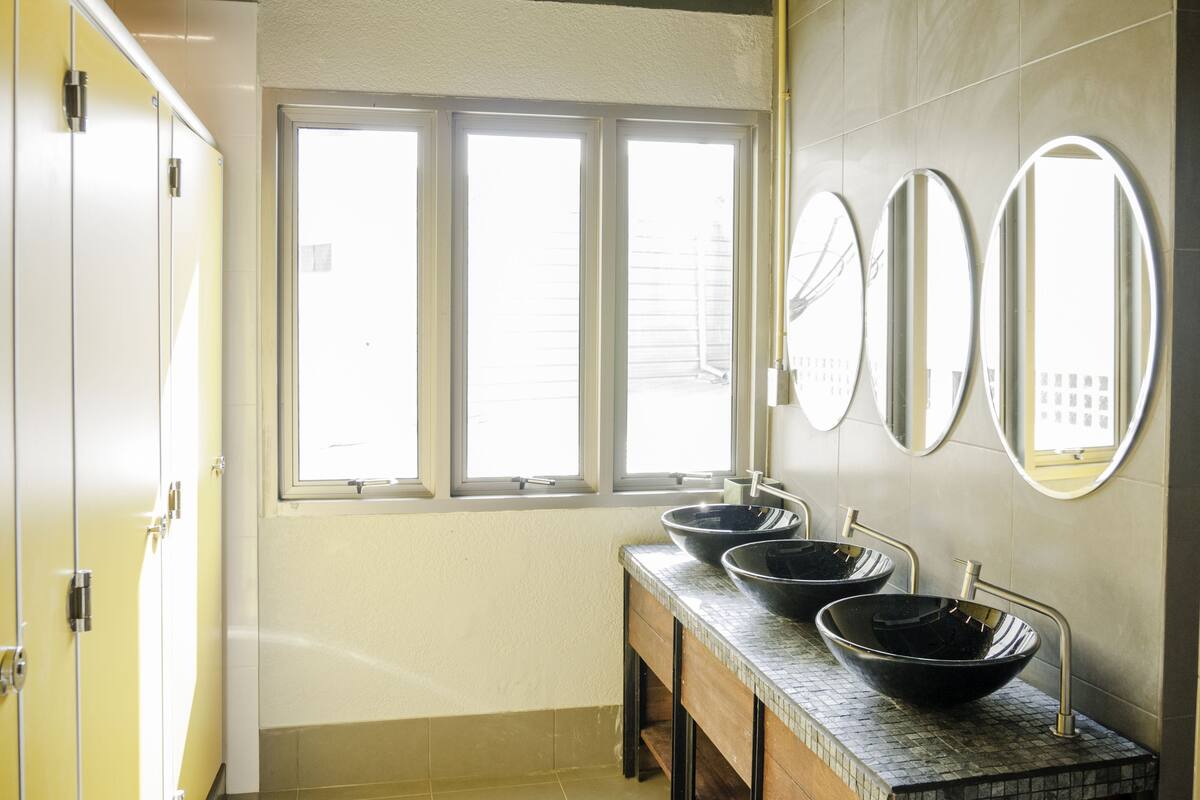 A bathroom with three sinks, a window, and a mirror.