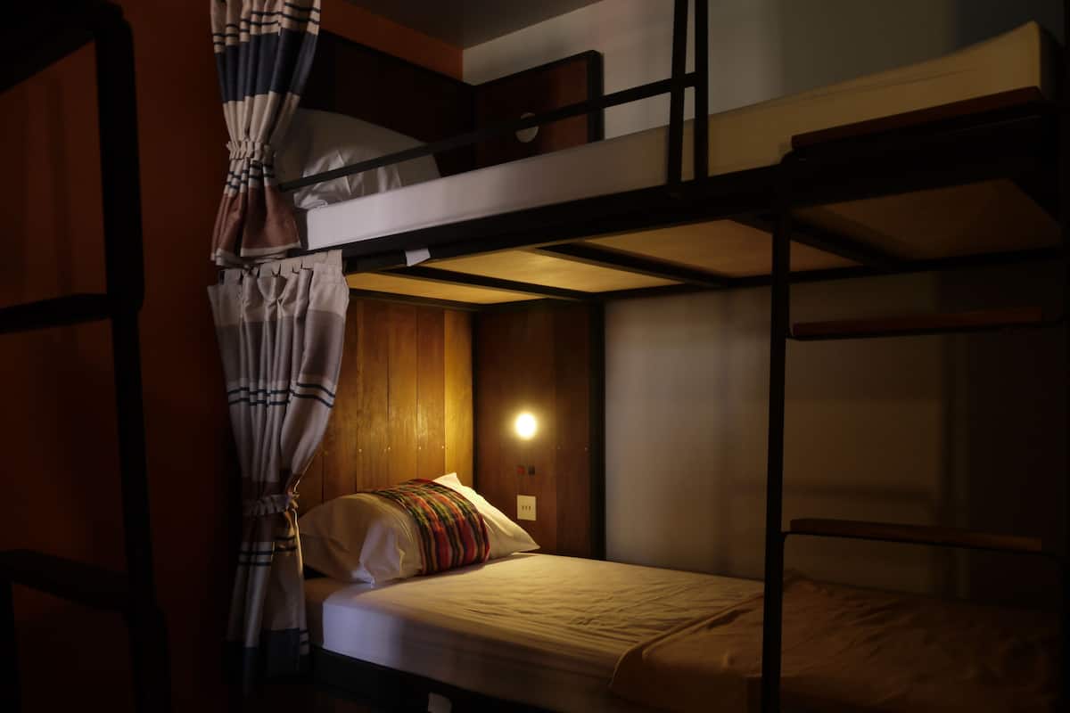 A bunk bed room with a curtain, a bedside table, and a wall-mounted light.