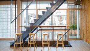A modern interior with a staircase, large windows, and wooden stools. - Whereder Poshtel - Hostel (Udon Thani)