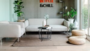 A modern living room with a sofa, a coffee table, and two potted plants. - Whereder Poshtel - Hostel (Udon Thani)