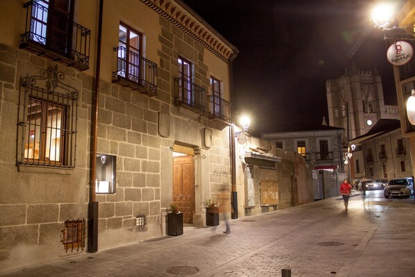 A historic street with stone buildings, a prominent tower, and a person walking. - El Encanto Hotel & Cafetería (Ávila)
