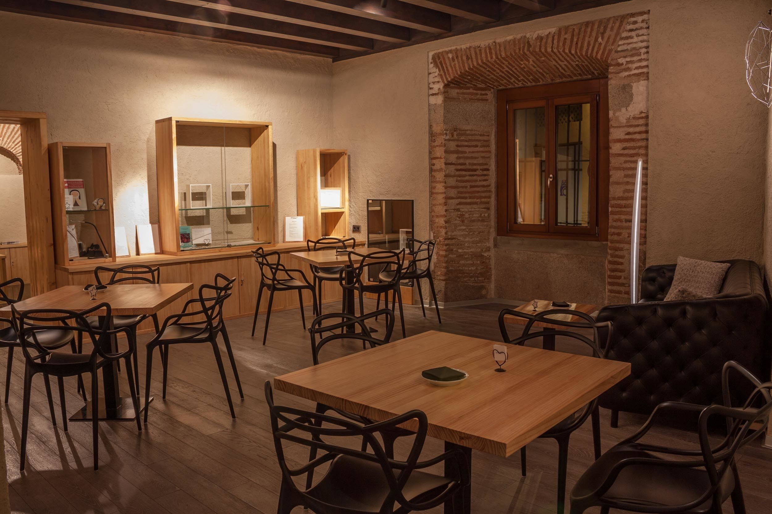 A dining area with wooden tables and chairs, a bar area with glass display cases, and a brick wall with a window.