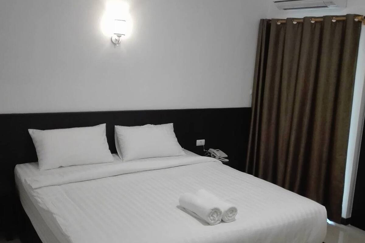 Habitación de hotel con cama, ropa de cama blanca, lámpara fijada a la pared, aire acondicionado y teléfono.