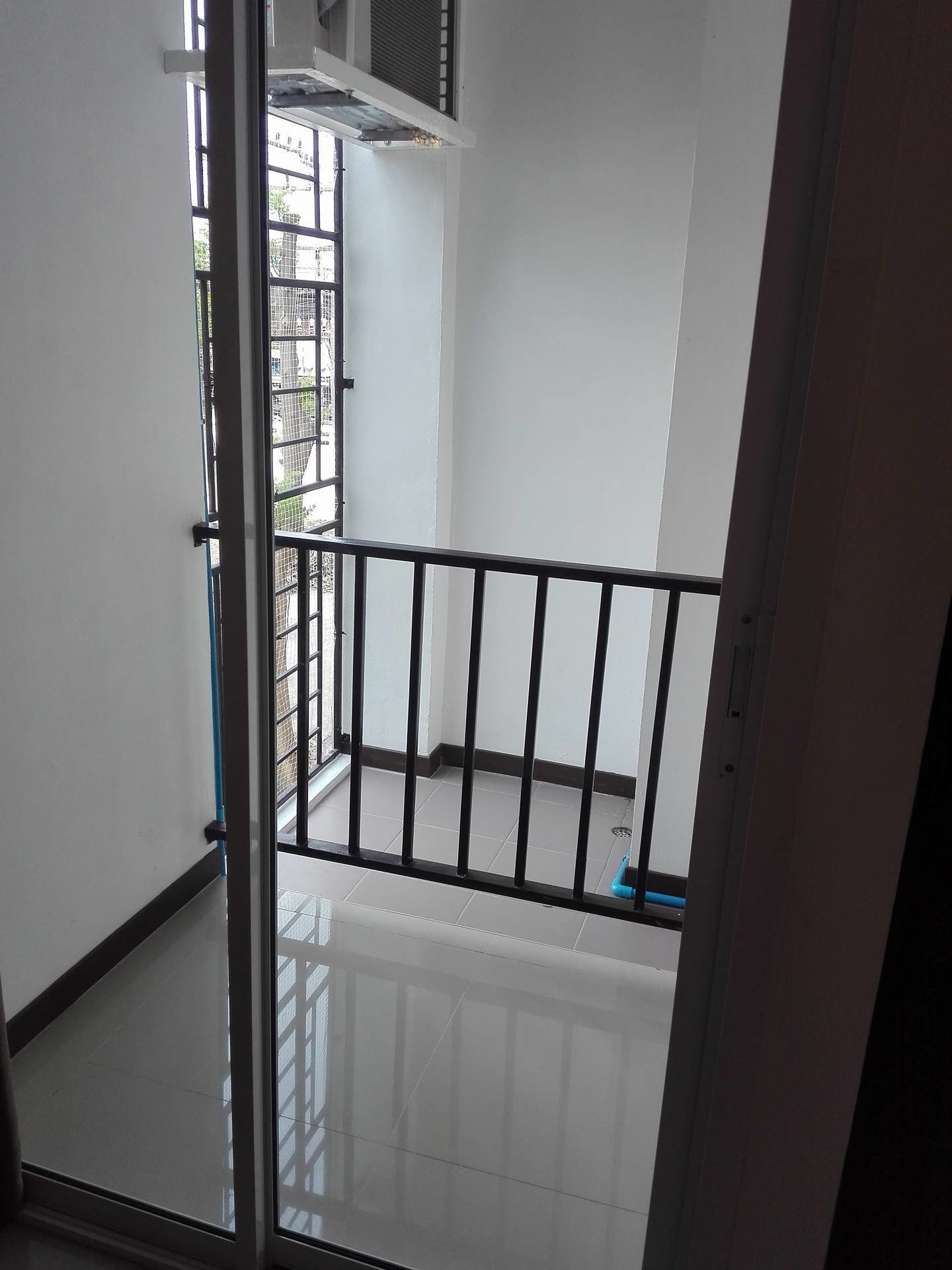 A view through a glass door into a balcony area with a metal railing, a tiled floor, and a white wall.